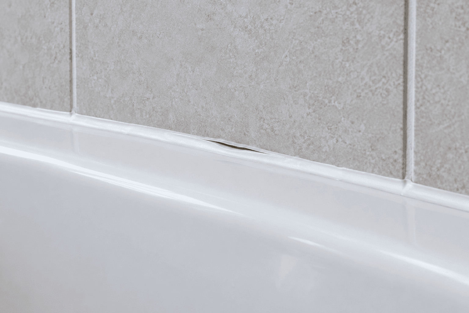 Illustration of a small lifted silicone edge where a bath rim meets a tiled wall.